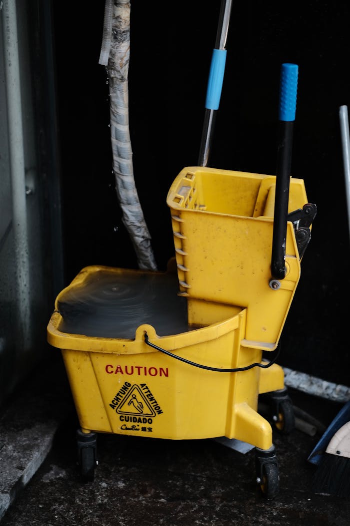 Close-up of a yellow mop bucket with caution sign, ideal for cleaning and maintenance themes.